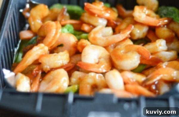 Air fryer basket filled with honey garlic shrimp and stir-fry vegetables, ready to cook
