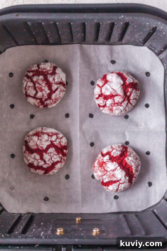 air fryer red velvet crinkle cookies baking in an air fryer on parchment paper, showing the sugar cracking beautifully