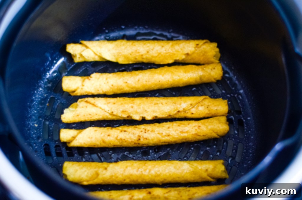 Air fryer basket filled with frozen taquitos during cooking