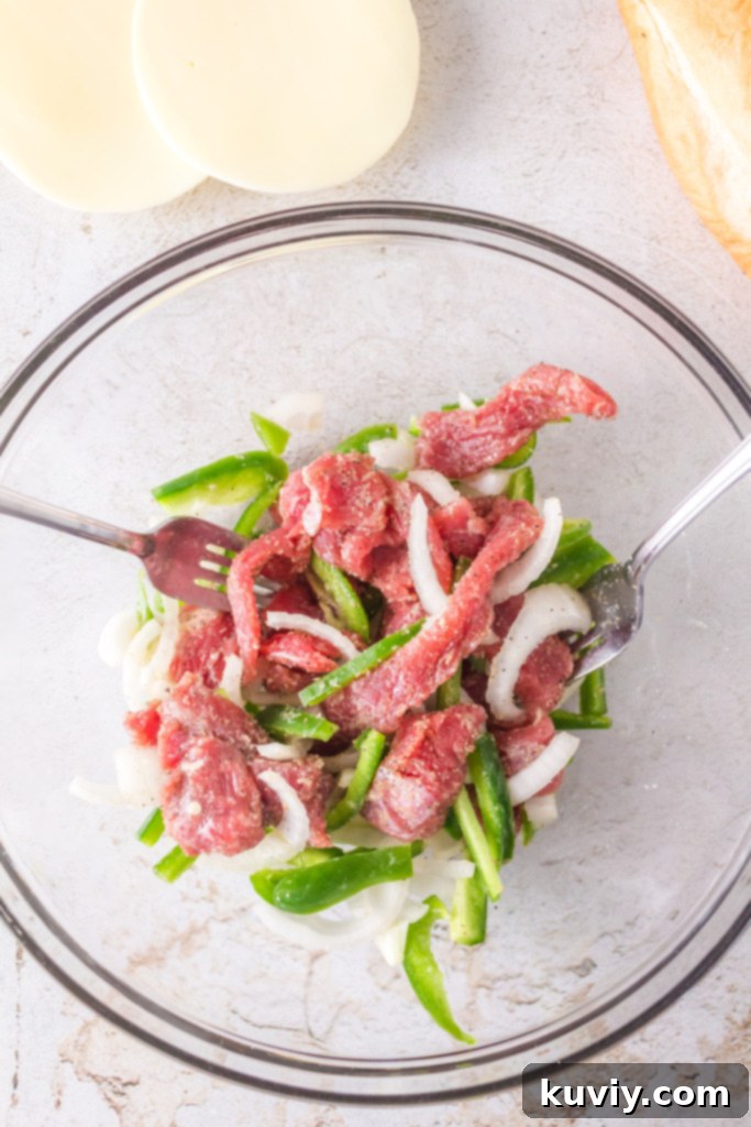 Thinly sliced raw Ribeye steak seasoned and ready for the air fryer, alongside sliced onions and bell peppers.
