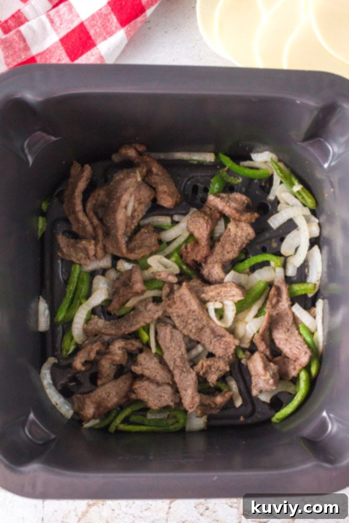 Seasoned steak, bell peppers, and onions in an air fryer basket, ready to be cooked.