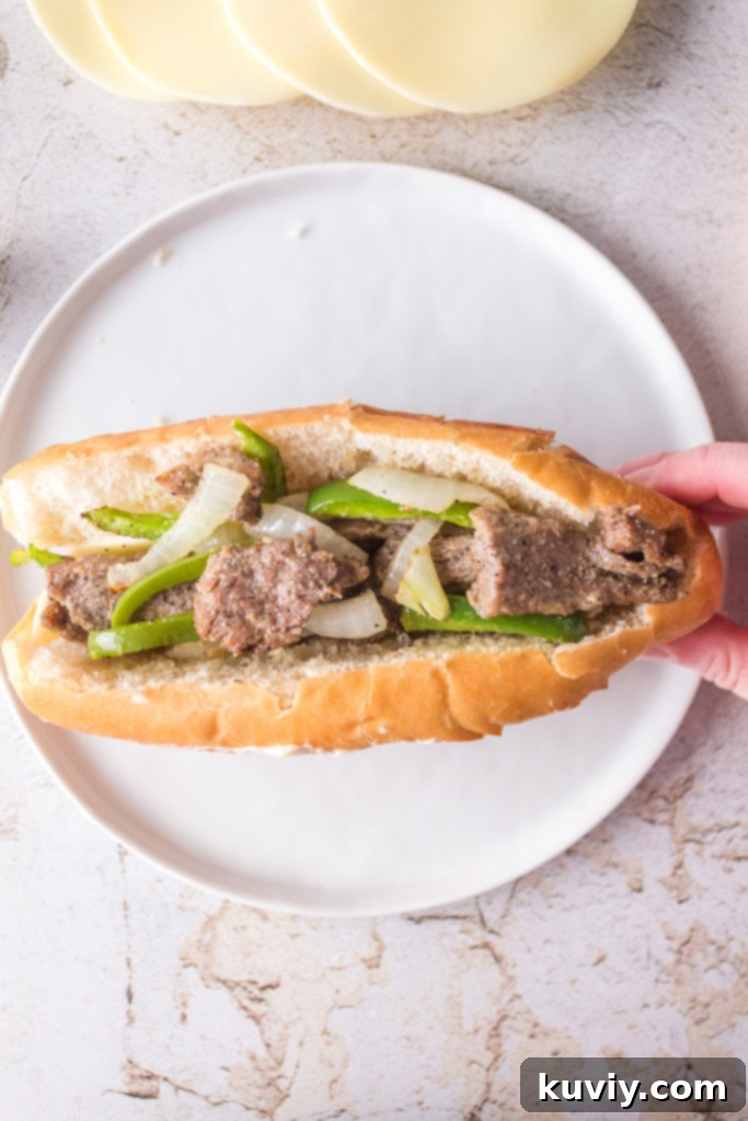Assembling Air Fryer Philly Cheesesteaks with melted provolone cheese, steak, and vegetables on hoagie rolls.