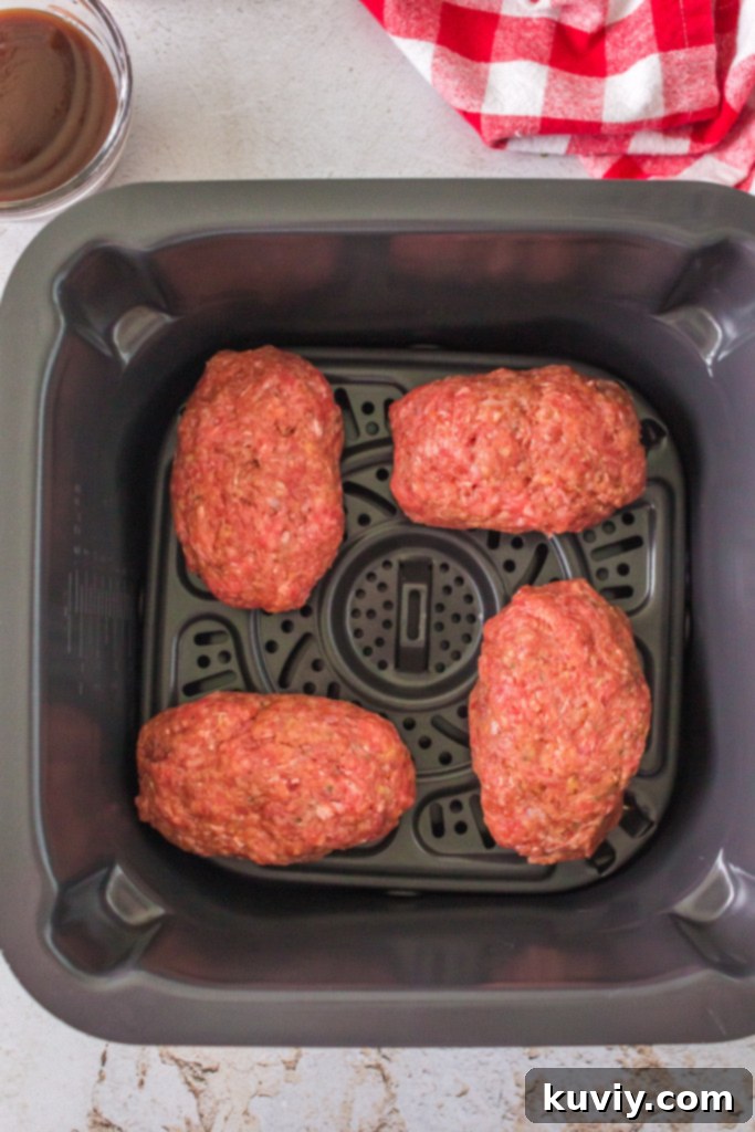 Four small, perfectly shaped mini meatloaves arranged in an air fryer basket, ready for cooking.
