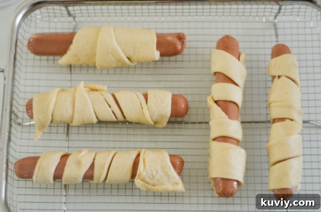 Crispy Air Fryer Crescent Hot Dogs 4 Hot dogs being wrapped with crescent roll strips